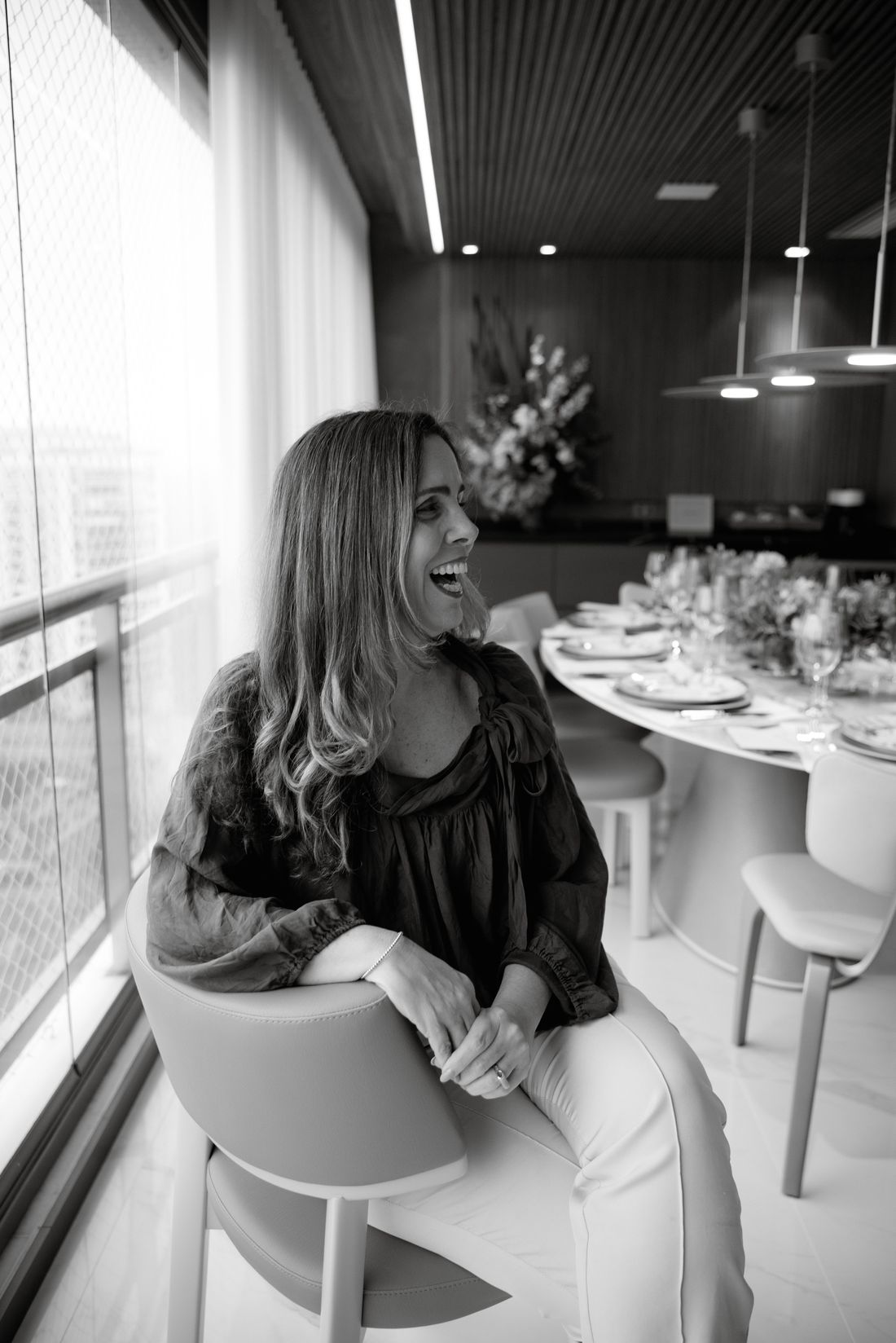 Denise Brante sorrindo, sentada à mesa de jantar