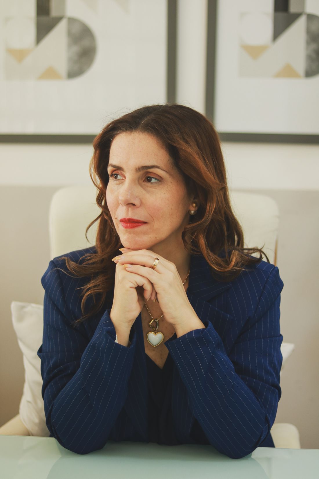 Denise Brante, de blazer azul-marinho, apoiando o queixo nas mãos